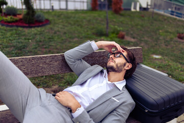 Young businessman resting on a bench in a park with his eyes closed
