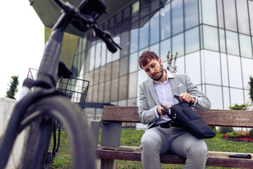 Young businessman placing his tablet into a bag while standing in a city environment with a bicycle.