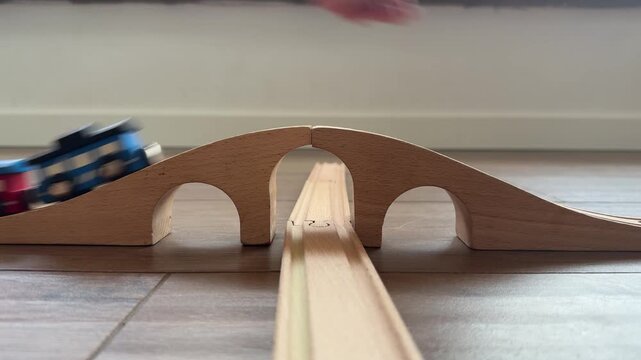 hand pushing wooden train on bridge, track on wooden floor, toy stores concept