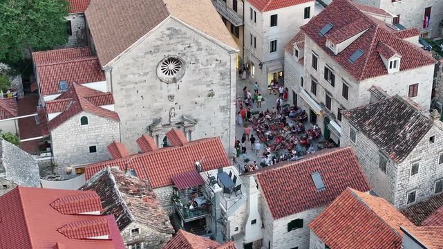 Drone aerial view of Trg Sveti Mihovil in the historic town of Omis at night showing illuminated stone buildings and a calm Mediterranean urban atmosphere