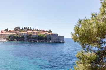 Obraz premium Panoramic view of a small island with an old coastal town, red tiled roofs and clear blue sea. Sunny summer day, Mediterranean landscape, travel and tourism concept. Island Sveti Stefan