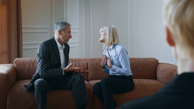 Senior Couple Having Conflict During Therapy Session With Marital Counselor In Office. Spouses Arguing And Blaming Each Other Having Meeting With Professional Psychologist. Selective Focus