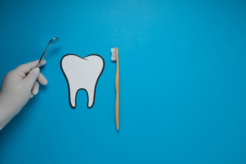 Dentist's hand with a mirror and fake tooth with a toothbrush, dental health, dentist's day.