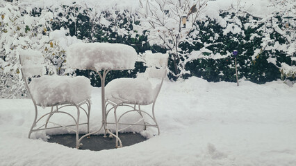 Winter garden landscape with snow accumulation on white metal chairs A bright and clean winter composition focusing on the contrast between the white snow and the garden's structures.