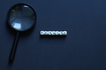 Magnifying glass beside letter tiles spelling examine on dark background, symbolizing research, inspection, analysis, and critical thinking with copy space.