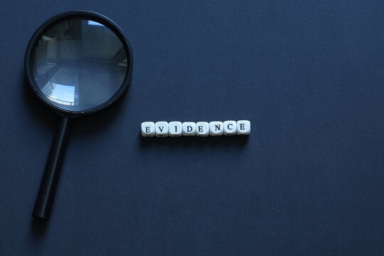 Letter tiles spelling evidence beside magnifying glass on dark background, representing proof, investigation, justice, research, and verification.