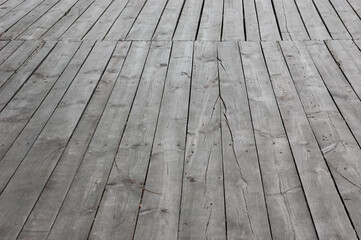 Old wooden walkway made of gray cracked boards with rusty nails and visible gaps, creating an abandoned atmosphere.