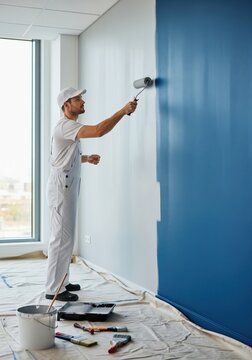 Professional painter painting office wall with roller brush for commercial renovation and maintenance service