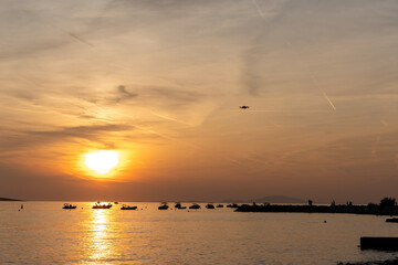 Golden sunset over calm sea with boats on horizon and drone flying in sky. Warm evening light, peaceful coastal atmosphere, travel destination and summer vacation background with copy space.