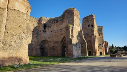 Rome, Italy - 14 January 2025. Sunlit ruins with arched recesses and brick walls stand near a walkway at the Baths of Caracalla, framed by bright winter sky.