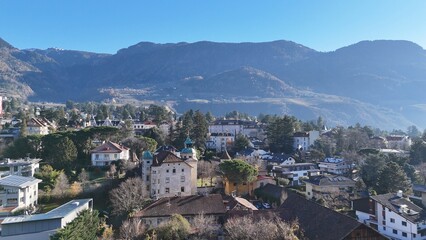 Obraz premium Alpine valley city with snowy mountains and moon aerial view Aerial view of alpine valley city with snowy peaks and visible moon in clear blue sky. Image works for winter tourism, evening mood and sce