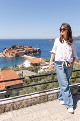 Adult woman wearing casual clothes standing on viewpoint terrace with sea and island in background, summer vacation lifestyle, travel and tourism concept, outdoor leisure, copy space