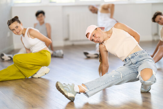 Happy teenage girl training hip-hop floor poses in dancehall during workout session in group