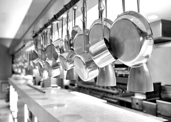 Black and white image of Side view of Copper pots and pans hanging in an industrial kitchen