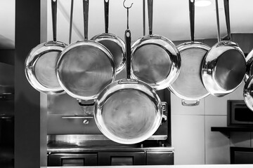 Black and white image of Copper pots and pans hanging in an industrial kitchen
