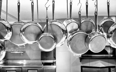 Black and white image of Copper pots and pans hanging in an industrial kitchen