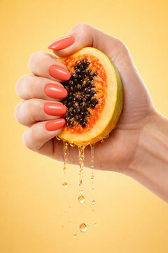 A woman's hand with coral nails squeezing a papaya, with juice dripping down against a vibrant yellow background. Highlighting freshness, manicure and fruit in a creative composition.