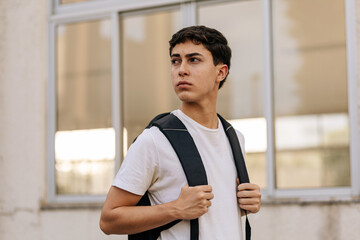 Teenage student standing outdoors with a backpack, looking away in an urban environment. Concept of youth, future, education, independence, lifestyle and daily routine