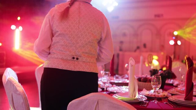 Waiter Serving Table in Restaurant with Stage Lighting in Background