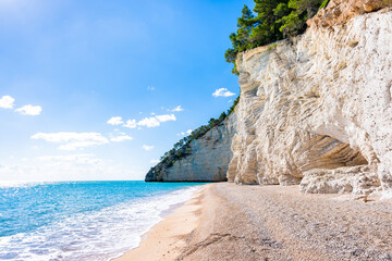 Fototapeta na wymiar Majestic white limestone cliffs towering over a quiet pebble Vignanotica beach on the Gargano coast, Apulia, Italy