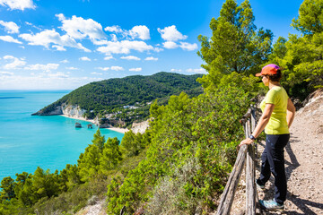 Female hiker admiring the turquoise sea and dramatic cliffs of Baia delle Zagare on the Gargano Peninsula, Apulia, Italy