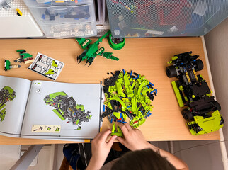 Obraz premium A child's hands assembling a green LEGO Technic car model according to the instruction manual on a wooden table: 04.05.2024- Ljubljana, Slovenia