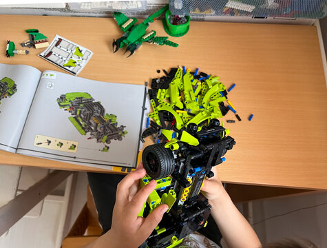 A child's hands holding a partially assembled LEGO Technic  car model, following the instruction manual on a des, flatlay: 04.05.2024- Ljubljana, Slovenia.