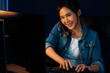 Smiling young beautiful Asian creative woman calling on phone desk to customer or coworker explaining creator project's profit while searching market analysis on pc at neon office at night. Stratagem.