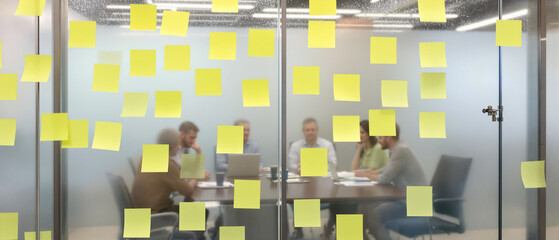Blurred team brainstorming behind glass wall covered with sticky notes in a modern office, focusing on collaboration and problem-solving during daytime.