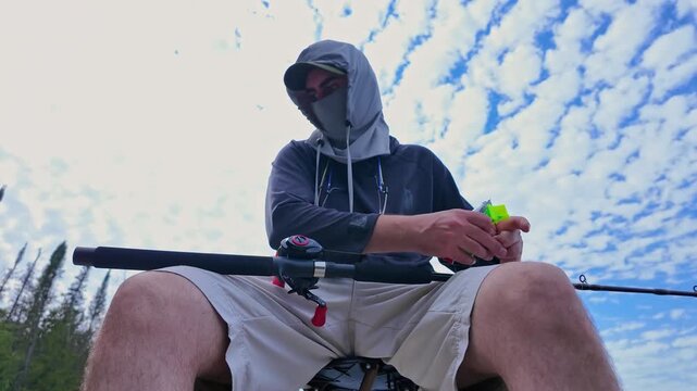 Angler changing top water lures on casting rod for fishing action technique to catch top water fish such as smallmouth or largemouth bass. View up from below. Sport angler in UV protective hood.