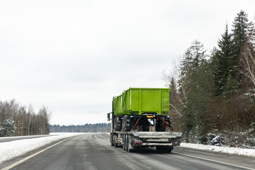 A tow truck transports two new green trailer for trucks along a highway. Heavy-duty transport and...