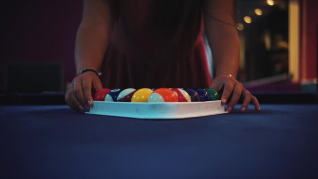 Close-up cinematic shot of a woman placing and arranging billiard balls on a pool table in a dimly lit bar. Concept of leisure, nightlife, entertainment, focus, and competitive games. Shallow depth of