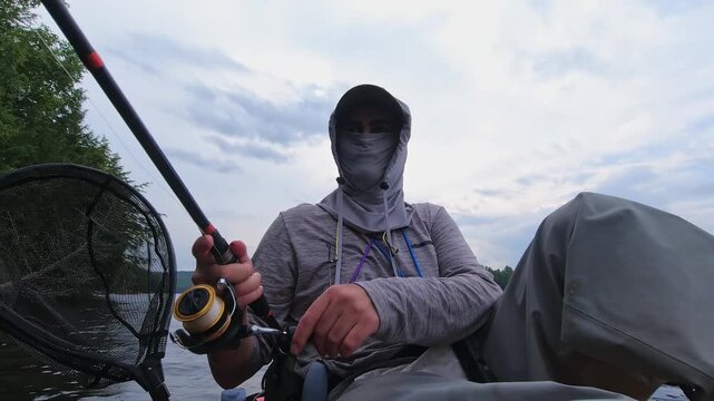 Kayak sport fishing. Angler enjoys kayak fishing at scenic coastline, casting his rod and reeling. Peaceful water shore and perfect setting at lake Simcoe, Ontario, Canada. Catch and release panfish.