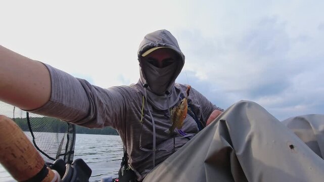 Kayak sport fishing. Angler enjoys kayak fishing at scenic coastline, casting his rod and reeling. Peaceful water shore and perfect setting at lake Simcoe, Ontario, Canada. Catch and release panfish.
