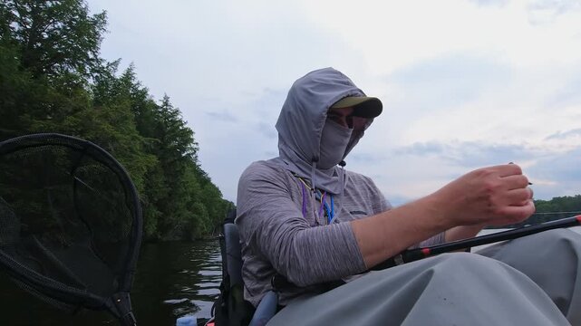 Angler put night crawler bait on fishing hook, line with bobber technique. Kayak sport fishing. Angler enjoys kayak fishing at scenic coastline. Peaceful water setting at lake Simcoe, Ontario, Canada