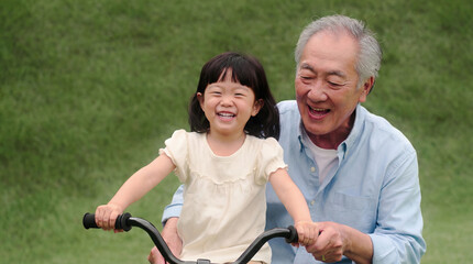 Obraz premium Cheerful senior Asian man teaching little granddaughter to ride bike in park