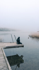Person sitting on a wooden pier by a calm sea on a foggy morning in Finland
