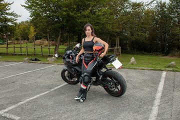 Obraz premium Young woman biker holding helmet next to sportbike