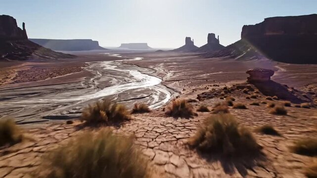 Epic aerial view of Monument Valley desert landscape with dried riverbed and iconic mesas under bright sunlight