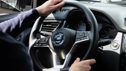 Male arms holds steering wheel while driving a motor car at city. Young man operating the automobile at urban road. Driver moving in his auto on route. Slow motion