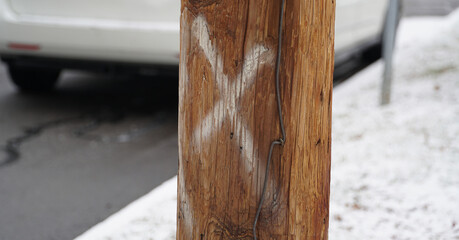 Close up of a wooden utility pole marked with a white spray-painted X for maintenance or removal