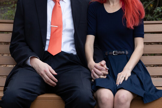 Couple sitting next to each other holding hands on bench in park