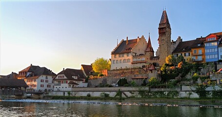 Golden Sunset Town, Serene Medieval Community By Glowing Castle And Reflective Water Under Soft Blue Sky