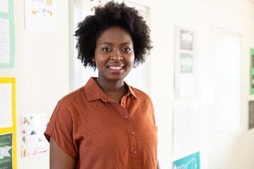 Woman standing and smiling in school classroom in rust-orange blouse with student drawings