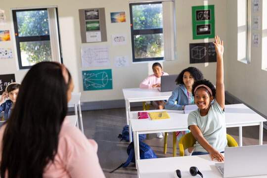 Female teens and teacher learning in class, front-right teen raising hand with laptop, copy space