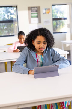 African American youth female students sitting in classroom using gray folio tablets at white desks