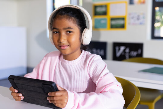 African American child sitting at school desk holding black tablet with white headset and pink top