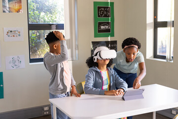 African American teenage students working at school table pointing at tablet, wearing VR headset