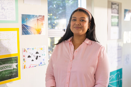 African American woman standing in classroom wearing pale pink shirt and headband, showing posters