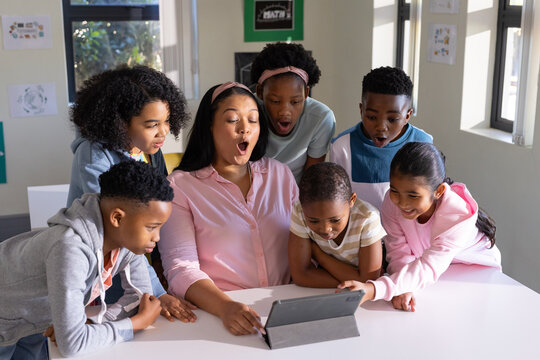 African American teacher in pink leading class with tablet on white table, children leaning in